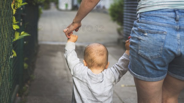 Learning to walk concept: Toddler is holding the hand of his mother, making his first steps. Close