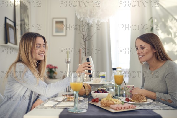 Smiling attractive young teenager showing her mother her mobile phone as they sit enjoying a
