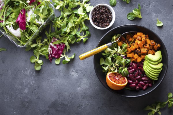 Quinoa salad in bowl with avocado, sweet potato, beans, herbs, orange on concrete rustic background