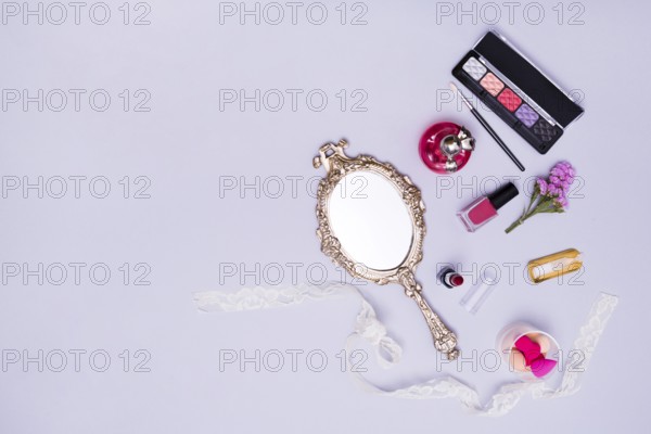 Vintage hand mirror lipstick nail varnish sponge perfume bottle eyeshadow palette purple background