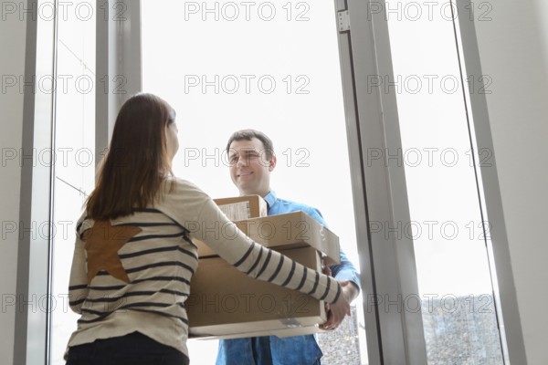 Fast and reliable service. Cheerful young courier giving a cardboard box to a young woman standing
