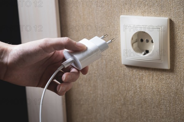 A young woman inserts a plug into a socket. A young woman plugs a charger or electrical appliance
