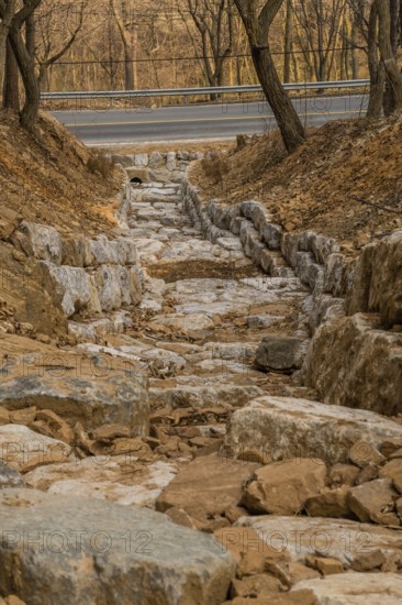 Drainage ditch constructed of large boulders on side of mountain on early spring afternoon in South