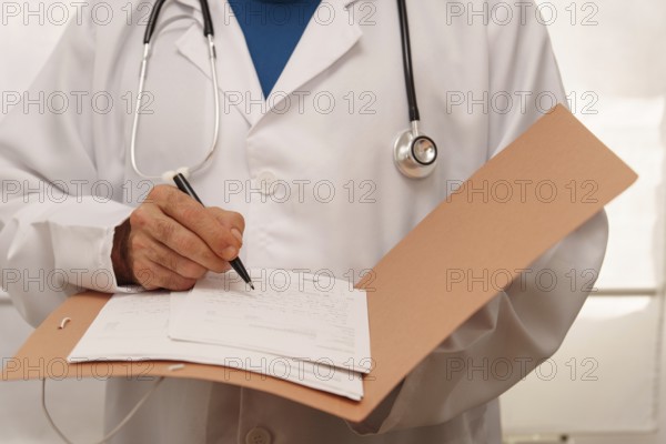 Unrecognizable doctor in white coat and stethoscope writing a prescription for a patient in his
