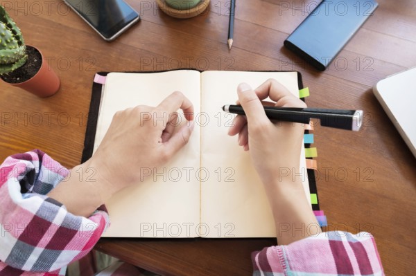 Young Caucasian attractive woman taking notes in her notebook while sitting in the kitchen at the