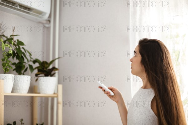 Young woman adjusts the temperature of the air conditioner using the remote control in room with a