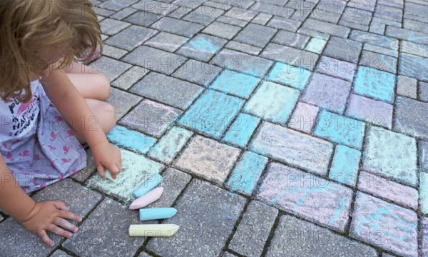 Child paints with colorful chalk on concrete pavement