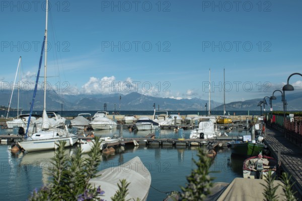 A harbour with numerous boats, mountains in the background and a clear sky, Sirmione, Lake Garda,
