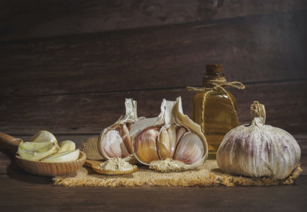 Whole, powdered and chopped garlic on a burlap cloth with a glass bottle with olive oil on a wooden