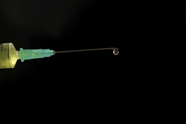 Syringe with needle with a drop of liquid coming out, isolated on black background and copy space