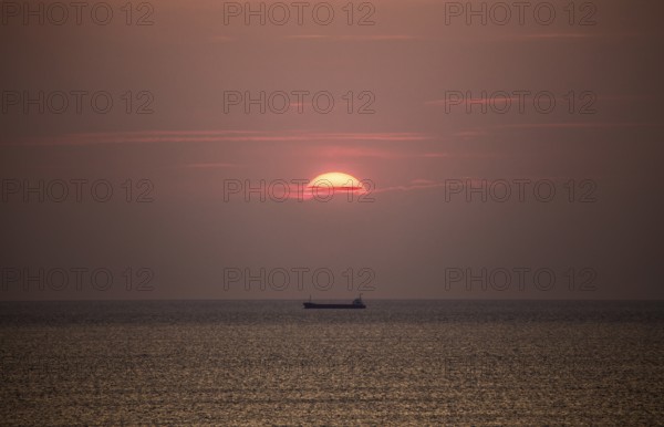 Cargo ship in the Mediterranean Sea under the evening sun, photographed from the beach near