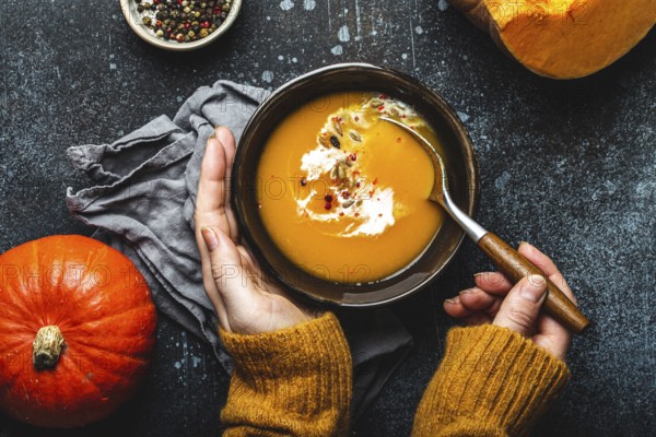 Woman in yellow knitted sweater eating a pumpkin cream soup on dark stone background with spoon