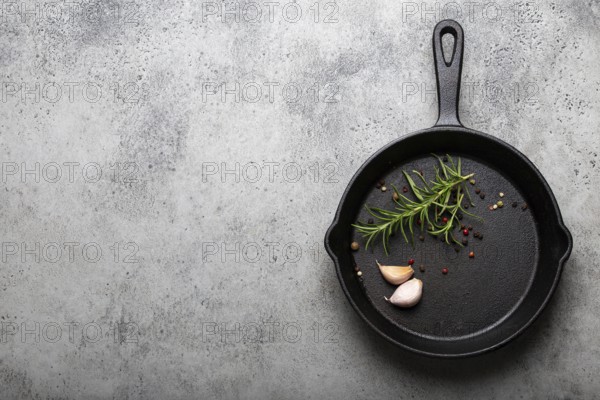 Black cast iron frying pan with ingredients for cooking: fresh green rosemary, raw garlic cloves