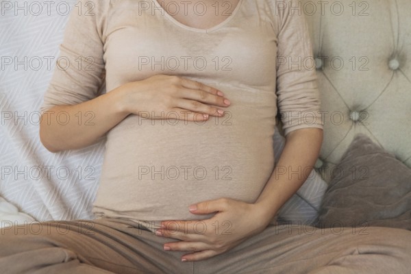 Cropped shot of pregnant woman holding belly while relaxing on couch at home, expectant mother