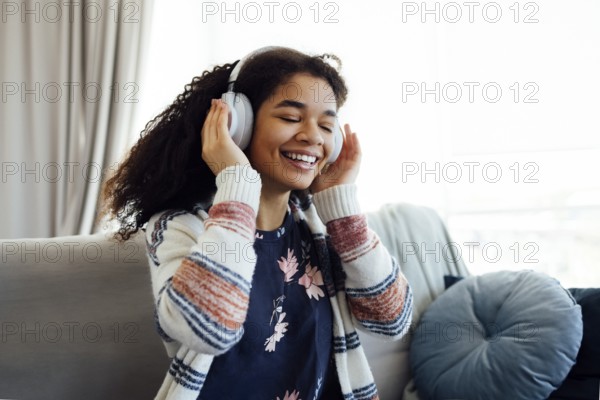 African millennial woman in orange sweater wearing white wireless headphones, listening music,