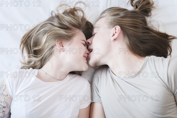 A top view of a molo pair of long-haired men and women laughing around fooling around in bed. A man