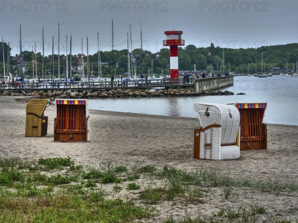 Beach with beach chairs, in the background a lighthouse and boats, overcast sky, eckernförde,