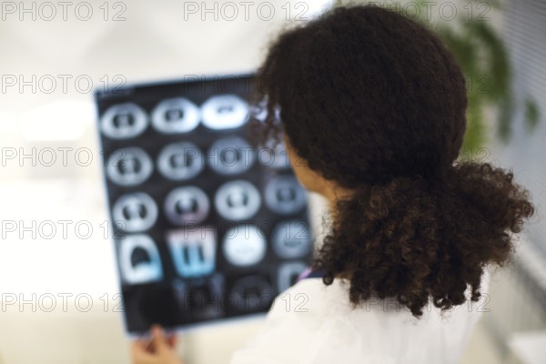 Rearview of ethnic female doctor analyzing X-ray or MRI scan while working in hospital, selective
