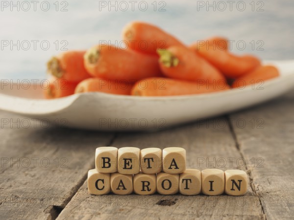 Wooden dices with the German words beta carotene and fresh carrots in the back, healthy eating
