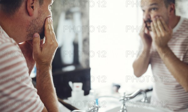 Millennial handsome man looking in mirror, applying moisturizing washing cream on cheeks in
