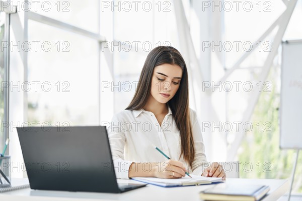 Pretty businesswoman with laptop and papers working at modern office. Woman signing contract and