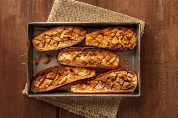 Roasted eggplants with garlic, shot from the top on a dark rustic wooden background with copy space