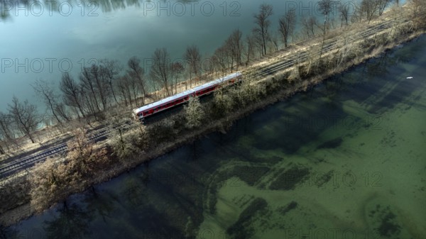 A red local railway runs on an embankment between two turquoise-coloured waters, drone shot, Upper