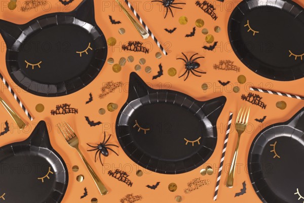 Black cat shaped Halloween party paper plates, bats and Happy Halloween text confetti on orange