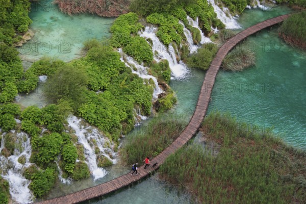 Wooden footbridge with hikers over turquoise ponds and waterfalls at Plitvice Lakes, Croatia,
