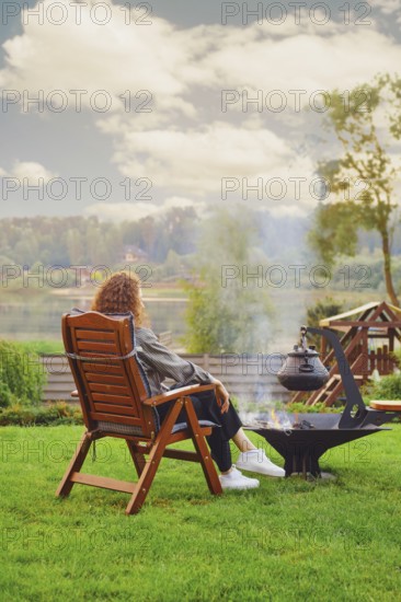 Unrecognizable young woman rests near fireplace at backyard in her country house