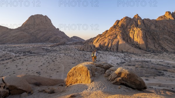 Couple on a mountain at sunset, summit of the Great Spitzkoppe and Pontoks in the background,