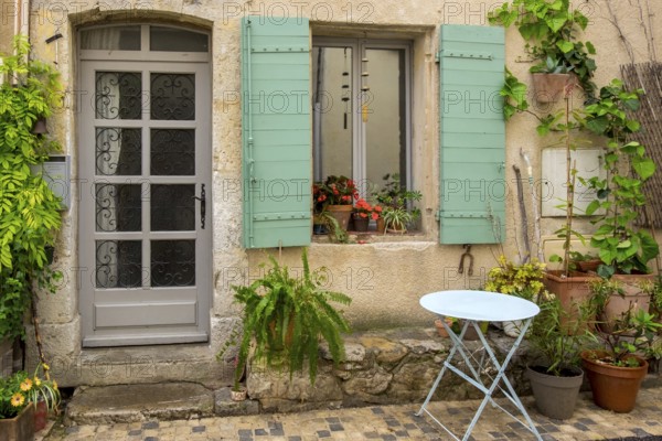 An old house façade with green shutters, numerous plants and a small round table, Vauvenargues,