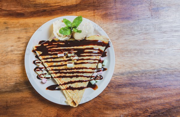 Top view of chocolate crepe with ice cream on wooden table. High angle view of chocolate crepe with