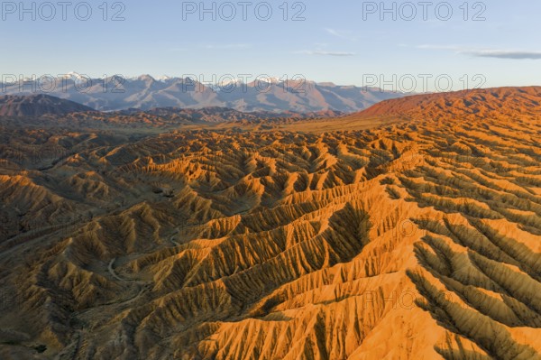 River bed runs through a landscape of eroded hills, badlands at sunset, mountain peaks of the Tian