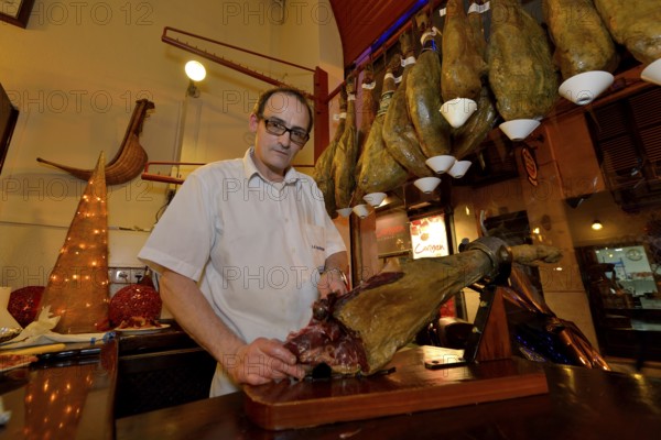 Waiter cuts ham in the "La Boveda" tapas bar, La Lonja district, Palma, Mallorca, Balearic Islands,