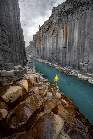 Tourist standing by the river in Stuðlagil Canyon, turquoise blue river between basalt columns,