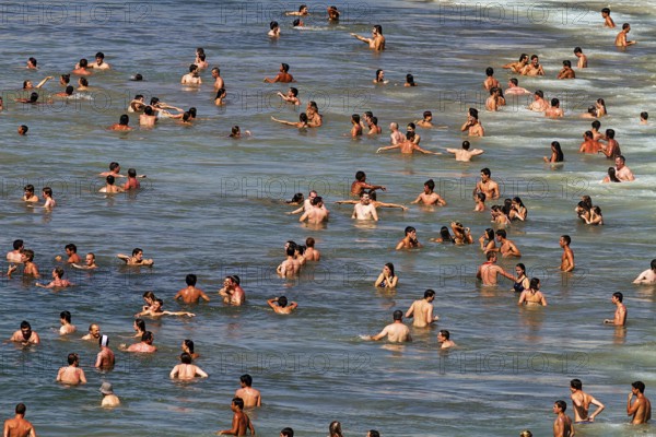 View from above on crowd on the beach, tourists swimming in the sea, enjoying cooling off, fun,