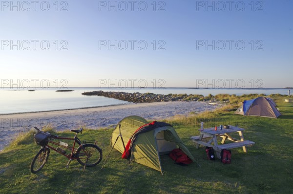 Camping on a quiet beach at dusk with tent, bike and picnic table, cycling holidays, adventure