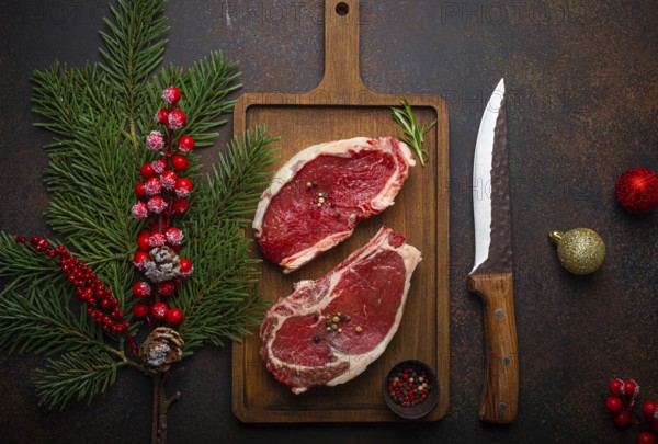 Two raw uncooked meat beef steaks on wooden cutting board with knife and seasonings on dark rustic