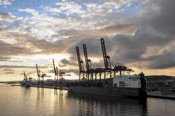 Harbour at sunset with cranes and a large ship, clouds in the sky are reflected in the water,