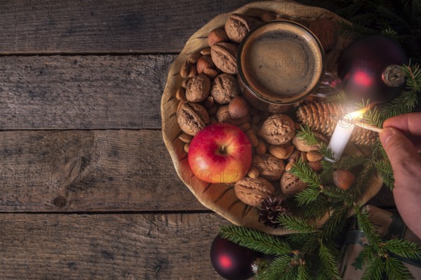 Christmas table with a wooden plate full with nuts, apples, a cup of coffee and green fir twigs,