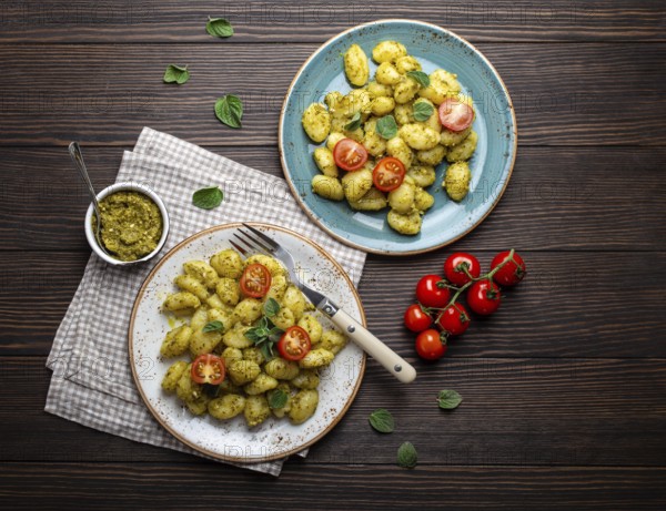 Gnocchi in plates with green pesto sauce, tomatoes and herbs on rustic wooden background, close up,