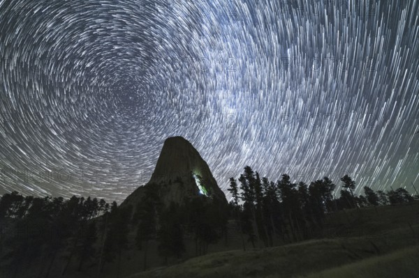 Star Trails over Devils Tower Butte at Night. Light Flare of Climbers on a Wall. Wyoming, USA,