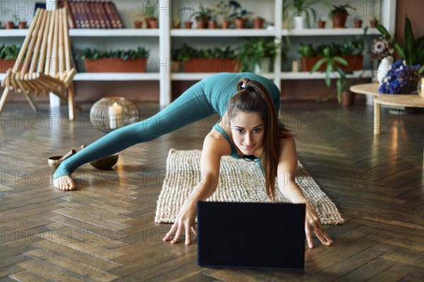 Young sporty woman practicing yoga at home watching online exercises on her laptop. Healthy