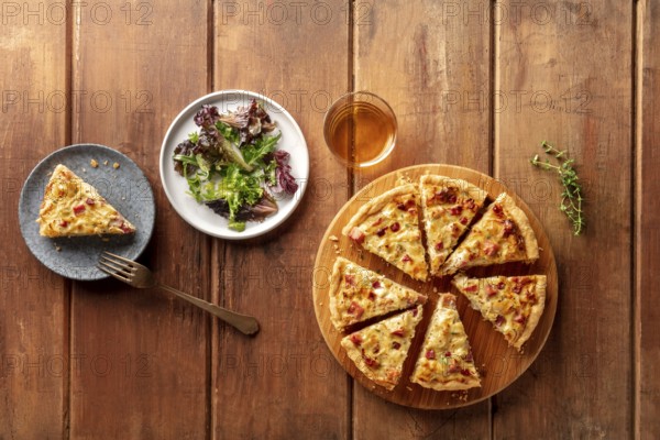 An overhead photo of a quiche with wine and mesclun salad leaves on a dark rustic wooden background