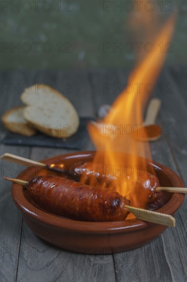Typical spanish tapa, chorizo on fire in an earthenware casserole with slices of bread in the