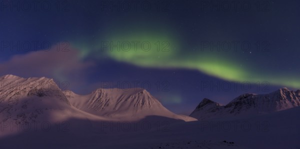 Northern Lights (Aurora borealis) over moonlit mountains in the valley Stuor Reaiddavaggi,