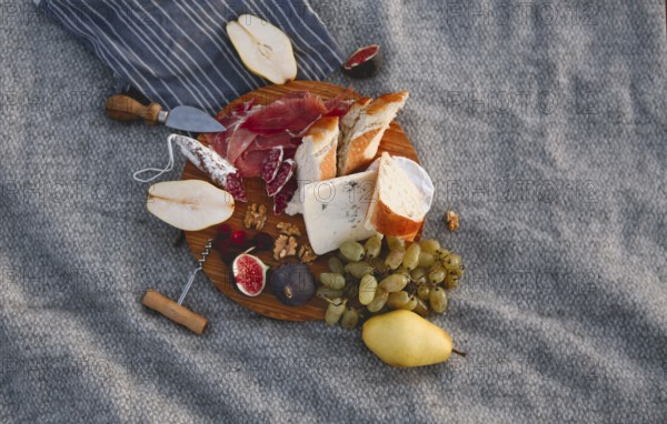 Top view of wooden board with pieces of bread pear figs nuts green grape and delicious cheese on