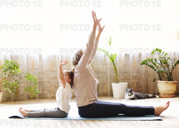 Mature woman and little girl sitting on mat in lotus pose and meditating while doing yoga in