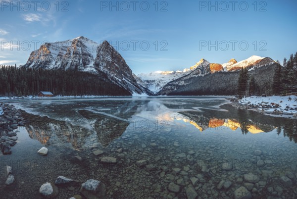 Peaceful lake reflecting snow-capped mountains and a cabin under a clear blue sky at sunrise, Lake
